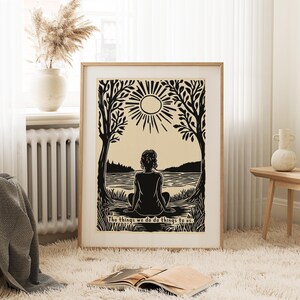 May include: A framed black and beige print depicts a person meditating by a lake under a sun. The artwork is surrounded by trees and includes the text, "The things we do do things to us."