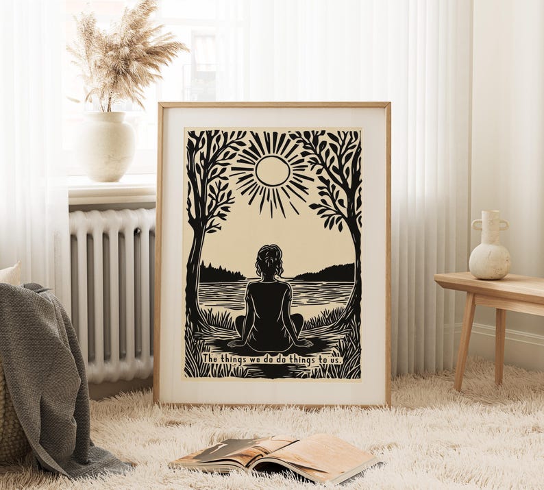 May include: A framed black and beige print depicts a person meditating by a lake under a sun. The artwork is surrounded by trees and includes the text, "The things we do do things to us."
