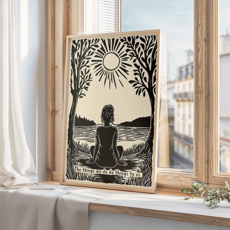 May include: A framed black and white art print featuring a silhouette of a person sitting by a lake, with a sun and trees in the background. The text "The things we do do things to us" is at the bottom.