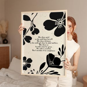 Puede incluir: Un cuadro enmarcado con dise&ntilde;os florales negros sobre un fondo crema. La impresi&oacute;n incluye el texto: "She chose quiet...Don't mistake it for compliance." El marco es de color madera clara.