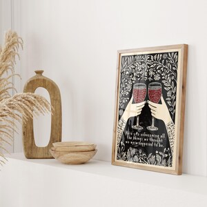 May include: A black and white illustration of two hands holding up wine glasses filled with red wine. The illustration is surrounded by a floral border and the text "Here's to unbecoming all the things we thought we were supposed to be."