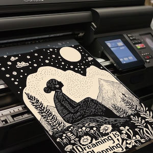 May include: Black and white illustration of a person sitting on a mountain with a moon and stars in the background. The text "Dreaming is  planning" is at the bottom of the image.