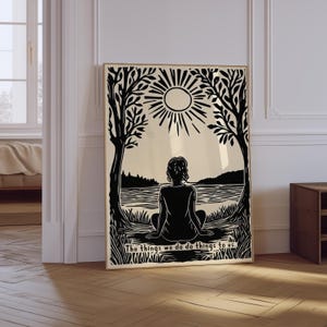 May include: Black and white art print featuring a person sitting by a lake, framed by trees and a sun. The text at the bottom reads, "The things we do do things to us."