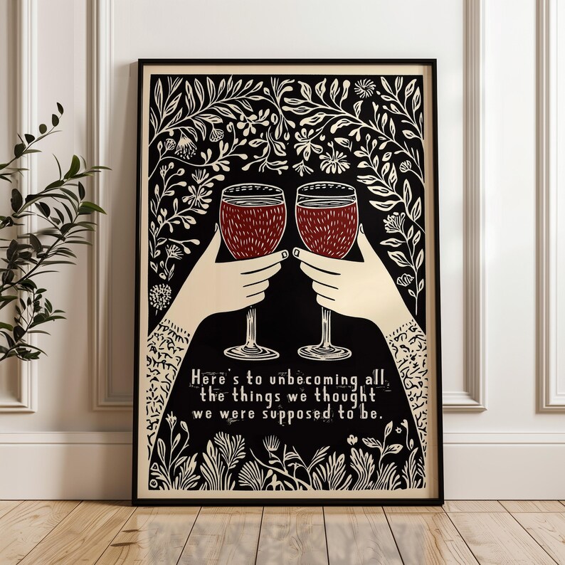 May include: Two glasses of red wine clink together in a black and white illustration with a floral border. The text reads "Here's to unbecoming all the things we thought we were supposed to be."