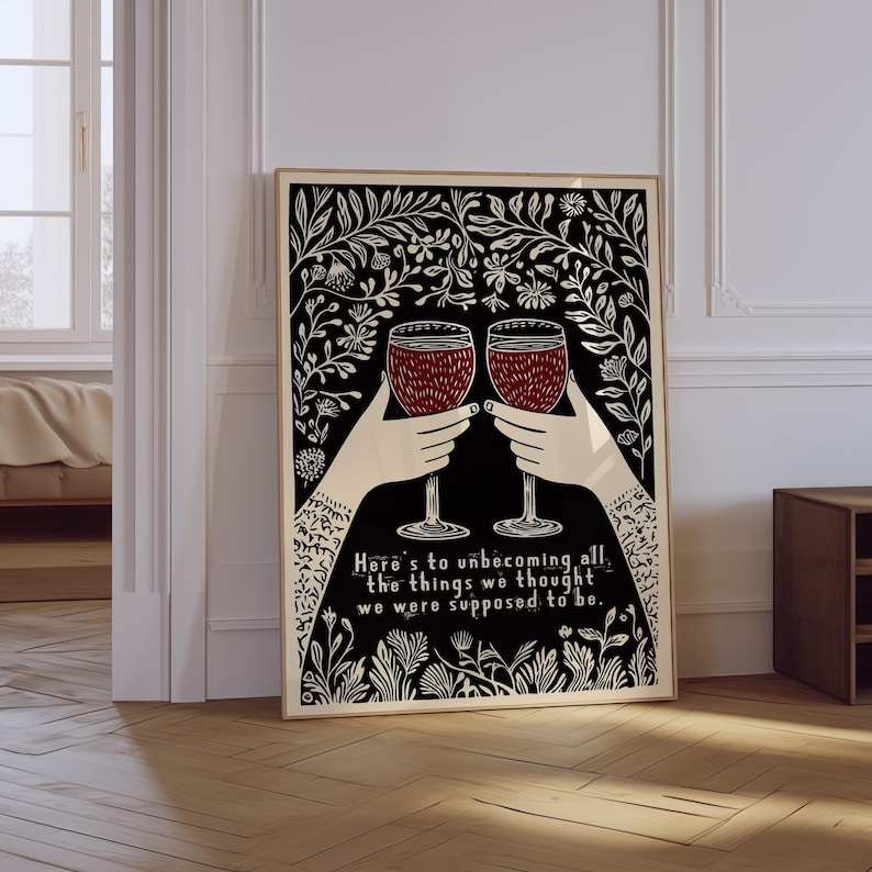 May include: Black and white illustration of two hands holding up wine glasses with red wine. The background is a black and white floral pattern. The text reads "Here's to unbecoming all the things we thought we were supposed to be."