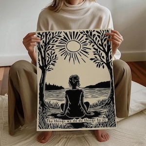 May include: Black and white art print featuring a serene landscape with a figure seated in meditation. The artwork includes a sun, trees, and the text "The things we do do things to us."