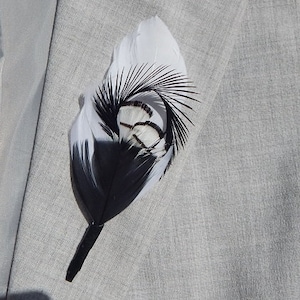 Może przedstawiać: Biało-czarna boutonnierka z piór z białą podstawą i czarnymi piórami na górze. Boutonnierka jest przymocowana do czarnej łodygi.