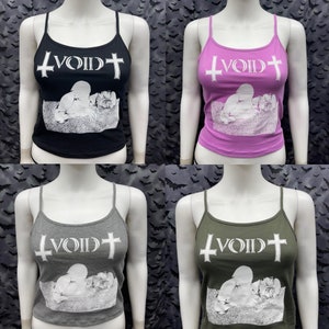 Può includere: Quattro canottiere con una stampa grafica di una persona sdraiata e il testo "VOID" con una croce su entrambi i lati. Le canottiere sono in nero, rosa, grigio e verde.