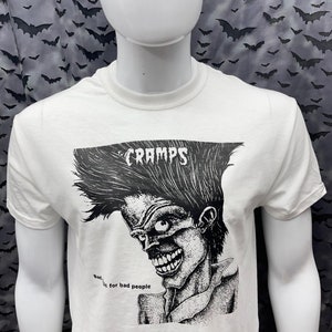 May include: White t-shirt with a black and white illustration of a person with a mohawk and the text "CRAMPS" and "Bad...ic for bad people".