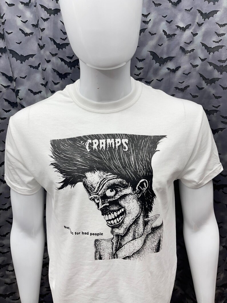 May include: White t-shirt with a black and white illustration of a person with a mohawk and the text "CRAMPS" and "Bad...ic for bad people".