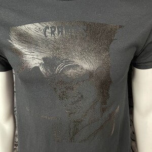 May include: Black t-shirt with a silver foil print of a person's face and the text "The Cramps" on the front.