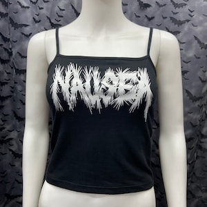 May include: Black spaghetti strap tank top with the word "NAUSEA" printed in white on the front. The word is stylized with jagged edges.