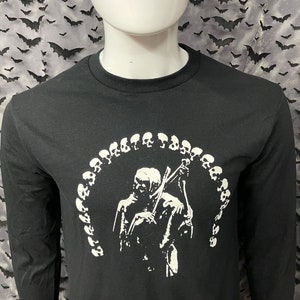 Könnte beinhalten: Schwarzes Langarm-T-Shirt mit einem weißen Motiv eines Skeletts, das Geige spielt, umgeben von einem Kreis aus Schädeln.