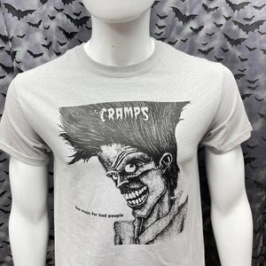 May include: A grey t-shirt with a black and white illustration of a person with a mohawk and the text "CRAMPS" and "Bad music for bad people".