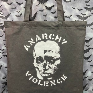 Puede incluir: Bolsa de lona negra con estampado blanco. El estampado presenta una calavera con las palabras "ANARCHY" arriba y "VIOLENCE" abajo.