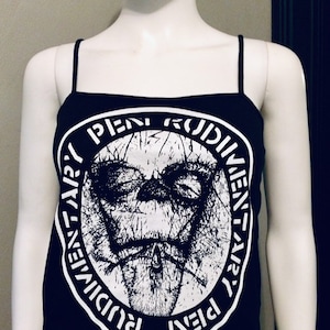 May include: Black tank top with a white graphic print of a face surrounded by a circle with the text "PIENI RUDIMENTI" repeated in a circular pattern.