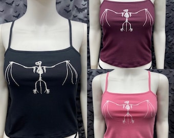 May include: Three sleeveless tops with a graphic print of a bat skeleton. The tops are black, burgundy, and pink.