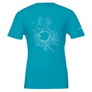 May include: A turquoise t-shirt with a white topographical map design. The map shows a circular formation with contour lines, possibly a volcanic crater. The shirt has short sleeves and a crew neck. The word "Crate" is printed on the right sleeve.