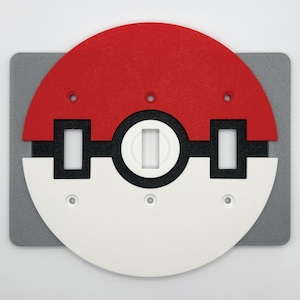 May include: A red, white, black, and gray decorative item, resembling a stylized ball. The top half is red, the bottom half is white, and a black band with white rectangles and a white circle divides the two halves. The item is mounted on a gray rectangular base.