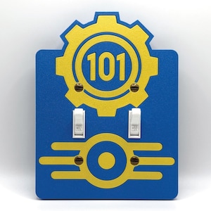 May include: Blue wall plate with a yellow gear and the number 101. Two white light switches are below the gear. The bottom of the plate has a yellow design with a circle in the middle. The switches are in the "ON" position.