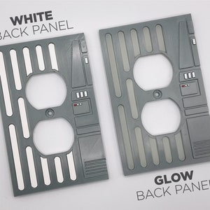 Puede incluir: Dos tapas de tomacorriente grises con un dise&ntilde;o de Star Wars. La tapa de la izquierda tiene acentos blancos y el texto "WHITE BACK PANEL". La tapa de la derecha tiene acentos grises y el texto "GLOW BACK PANEL".