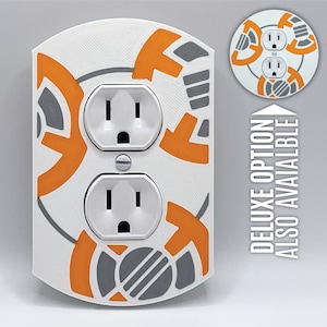 May include: White electrical outlet cover with a custom design featuring an orange and gray pattern. The design resembles the character BB-8 from the Star Wars franchise. The text "DELUXE OPTION ALSO AVAILABLE" is printed on the right side of the image.