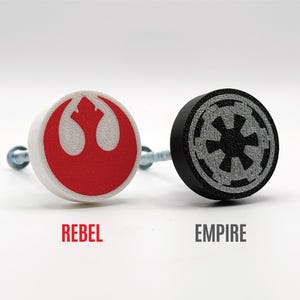May include: Two Star Wars themed knobs, one with a white background and a red Rebel Alliance symbol, the other with a black background and a gray Imperial symbol.  The knobs are attached to screws.