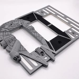 May include: A gray plastic light switch cover with a 3D printed design of the Millennium Falcon spaceship from Star Wars. The cover has two switch openings.