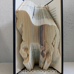 May include: A book art sculpture of a horse, folded from the pages of a book. The book is bound in black and the pages are cream colored. The sculpture is titled "Thebookmagician".