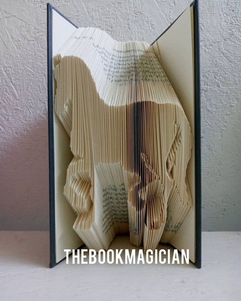 May include: A book art sculpture of a horse made by folding the pages of a book. The book is open and the sculpture is visible. The book has a dark blue cover and the text "THEBOOKMAGICIAN" is printed on the bottom of the book.
