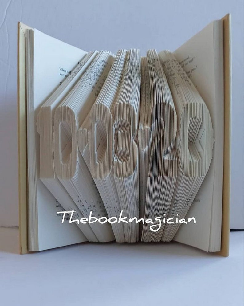 May include: A book art sculpture shaped like the numbers 10.03.2020. The book is folded and the pages are cut to create the shape. The book is open and the spine is visible. The text "Thebookmagician" is printed on the bottom of the book.