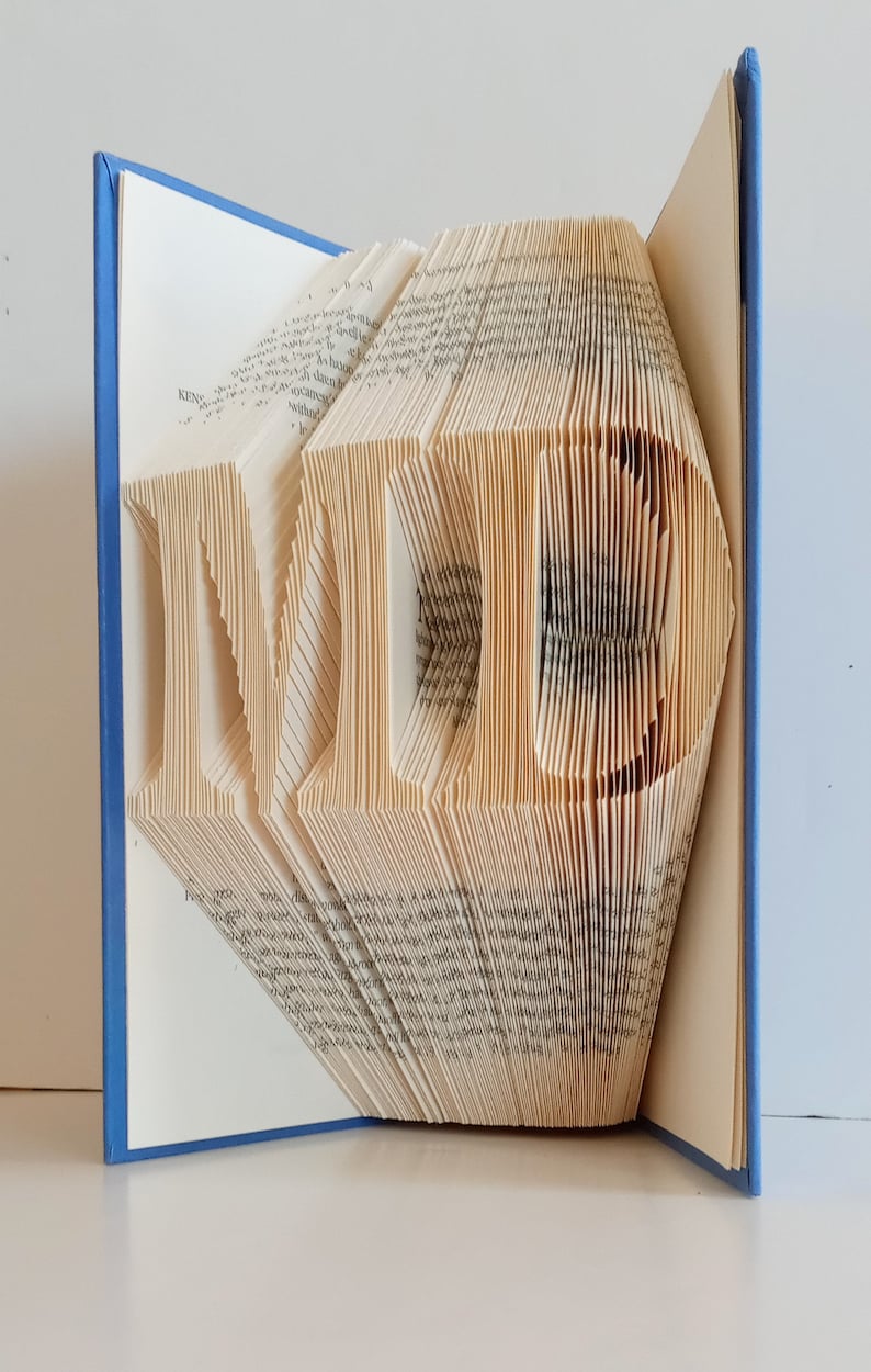 May include: A book with pages folded to create the letters "MD" in a 3D design. The book has a blue cover.