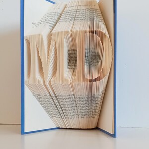 May include: A book with the letters "MD" folded into the pages. The book has a blue cover.