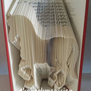 May include: A book folded into the shape of a horse. The book is open and the pages are folded to create the shape of the horse. The book is red and the horse is white. The text "thebookmagician" is printed on the bottom of the book.