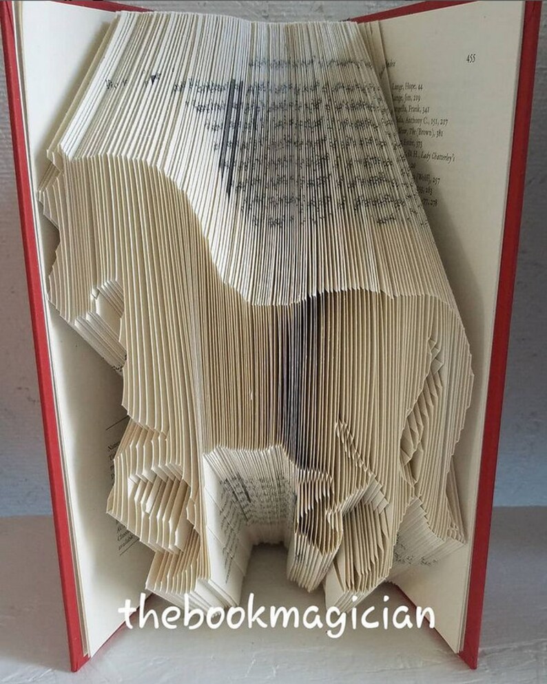 May include: A book folded into the shape of a horse. The book is open and the pages are folded to create the shape of the horse. The book is red and the horse is white. The text "thebookmagician" is printed on the bottom of the book.