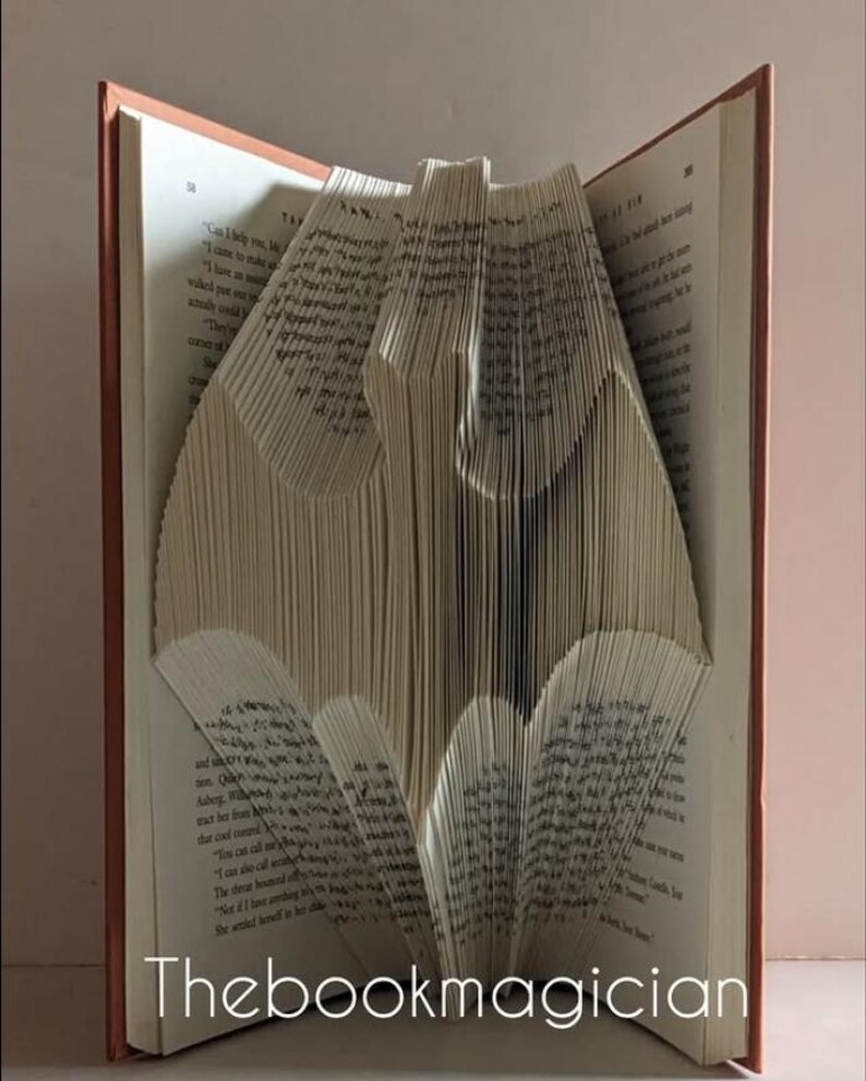 May include: A book folded into the shape of a Batman logo. The book is open and the pages are folded to create the shape. The book is brown with a white spine.