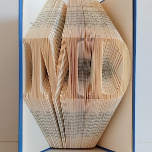 May include: A book with the word "MED" folded into the pages. The book has a blue cover and is open to reveal the folded pages.