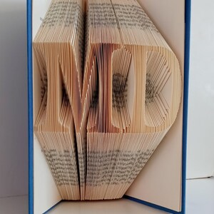 May include: A book with the word "LOVE" folded into the pages. The book is blue and the pages are cream colored.