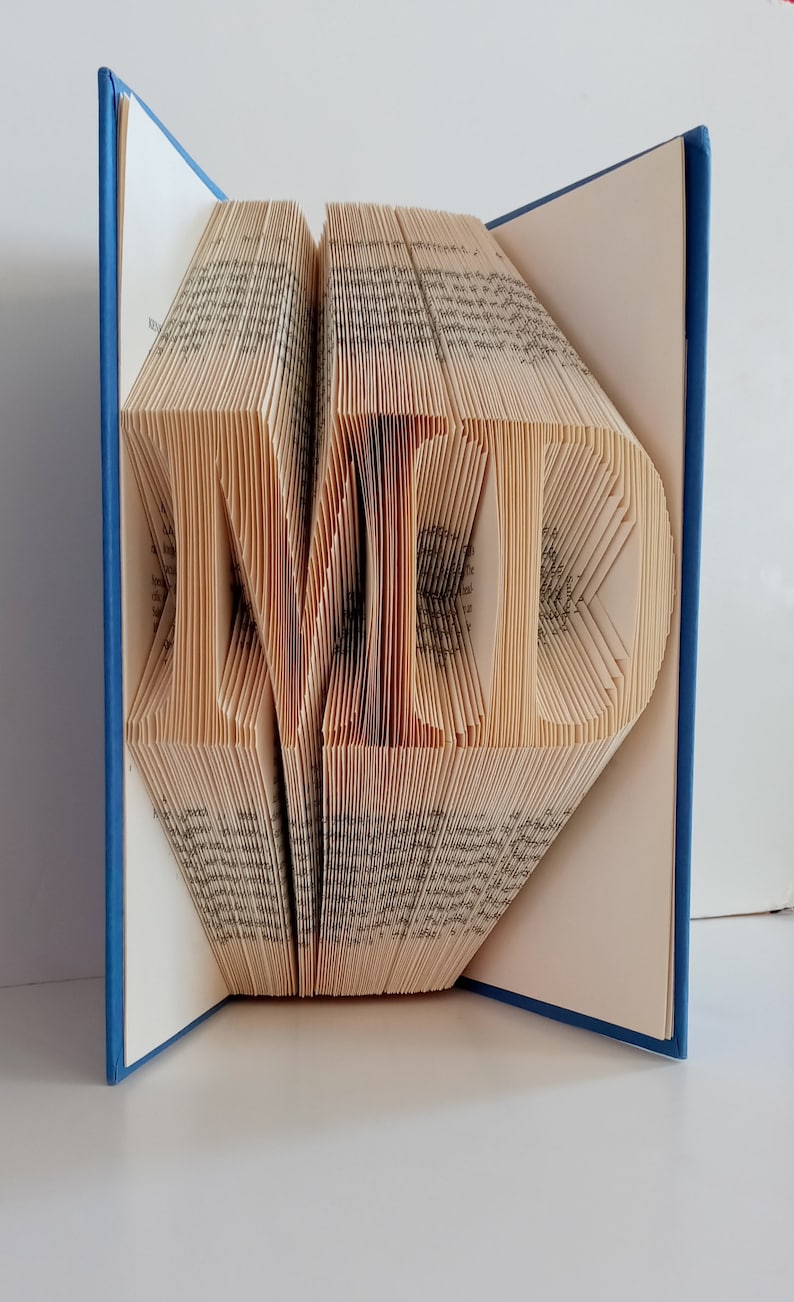 May include: A book with the word "LOVE" folded into the pages. The book is blue and the pages are cream colored.