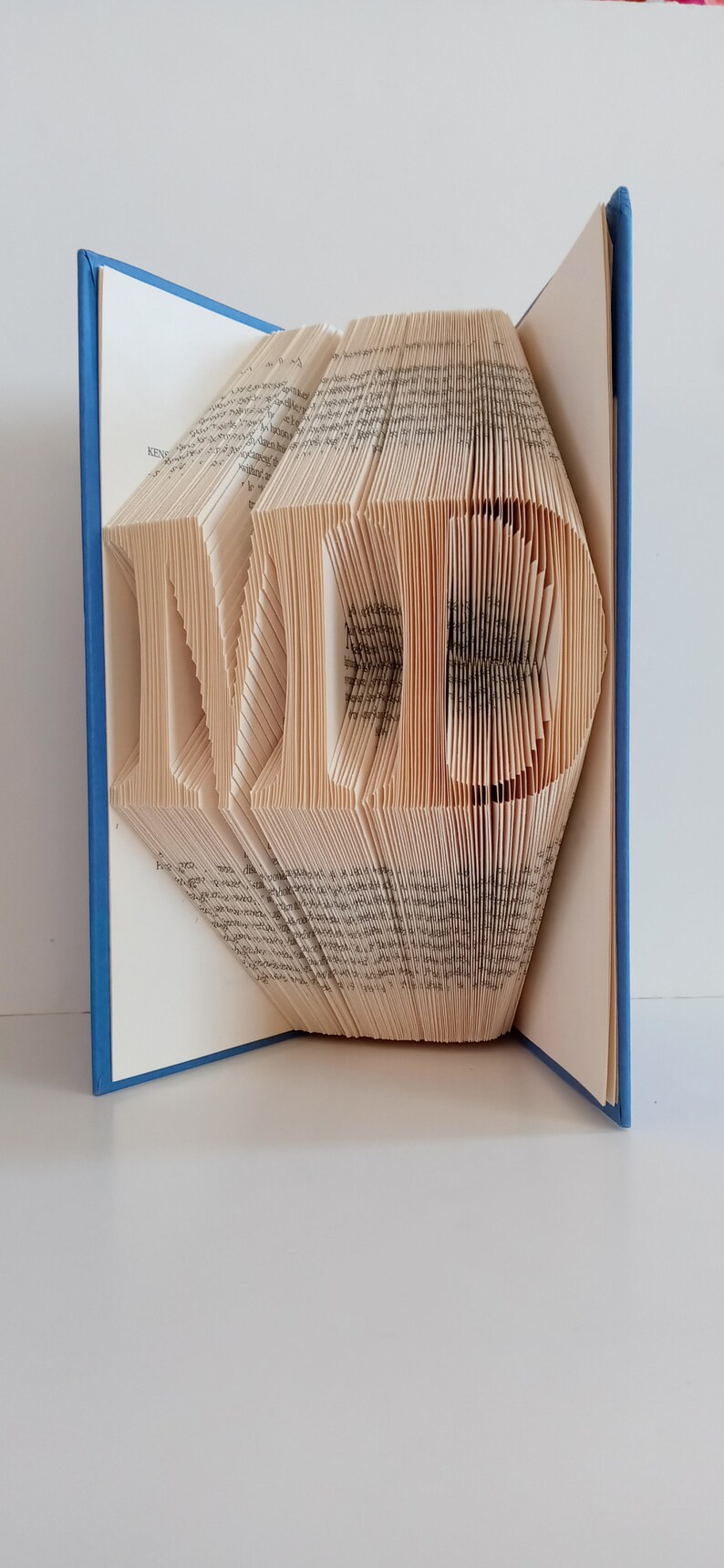 May include: A book with the letters "MD" folded into the pages. The book has a blue cover.