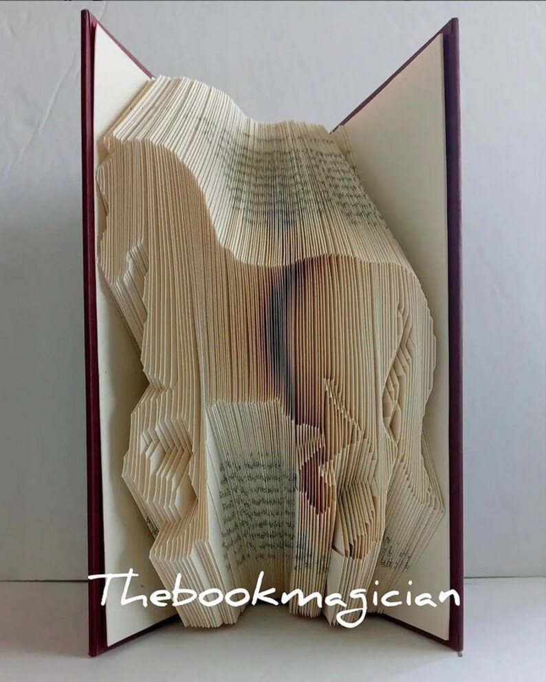 May include: A book art sculpture of a horse, folded from the pages of a book. The book is bound in a burgundy cover and the sculpture is standing upright. The text "Thebookmagician" is visible on the bottom of the book.