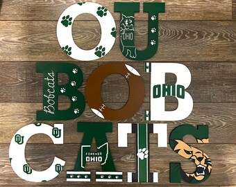 May include: Wooden letters spelling "OU BOBCATS" in white, green, and brown. The "O"s are white with green paw prints. The "B" is green with "Bobcats" written on it. The "O" is brown like a football.