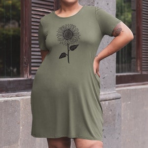 May include: A woman wearing a green short-sleeved dress with a black sunflower graphic print. She is standing on a sidewalk in front of a building.