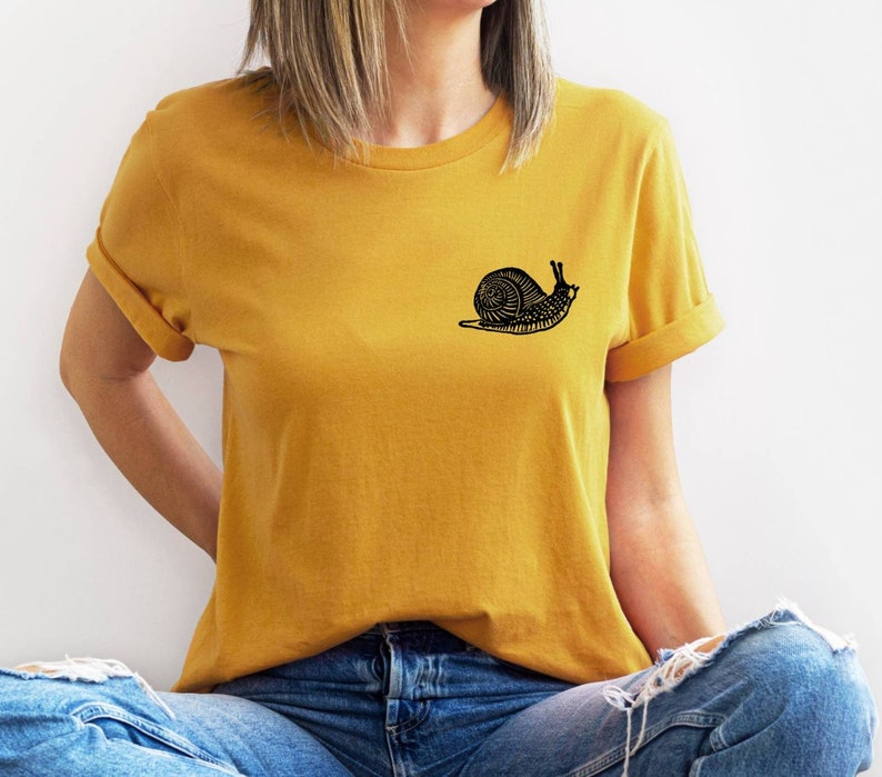 May include: A mustard yellow t-shirt with a black snail graphic on the left chest.