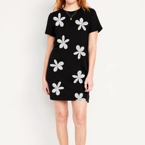 May include: A black t-shirt dress with a white daisy print. The dress has short sleeves and a round neckline.