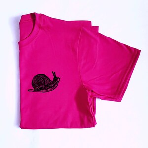 May include: A pink t-shirt with a black snail graphic design.
