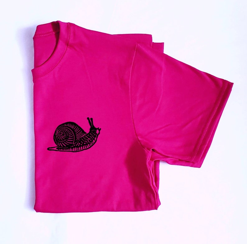 May include: A pink t-shirt with a black snail graphic design.