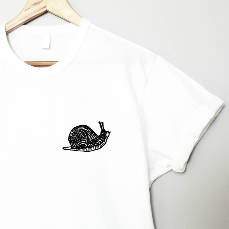 May include: White t-shirt with a black silhouette of a snail printed on the front.