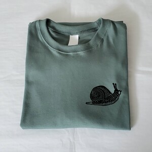 May include: A green t-shirt with a black snail graphic printed on the front.