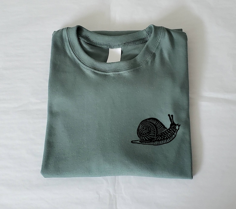 May include: A green t-shirt with a black snail graphic printed on the front.